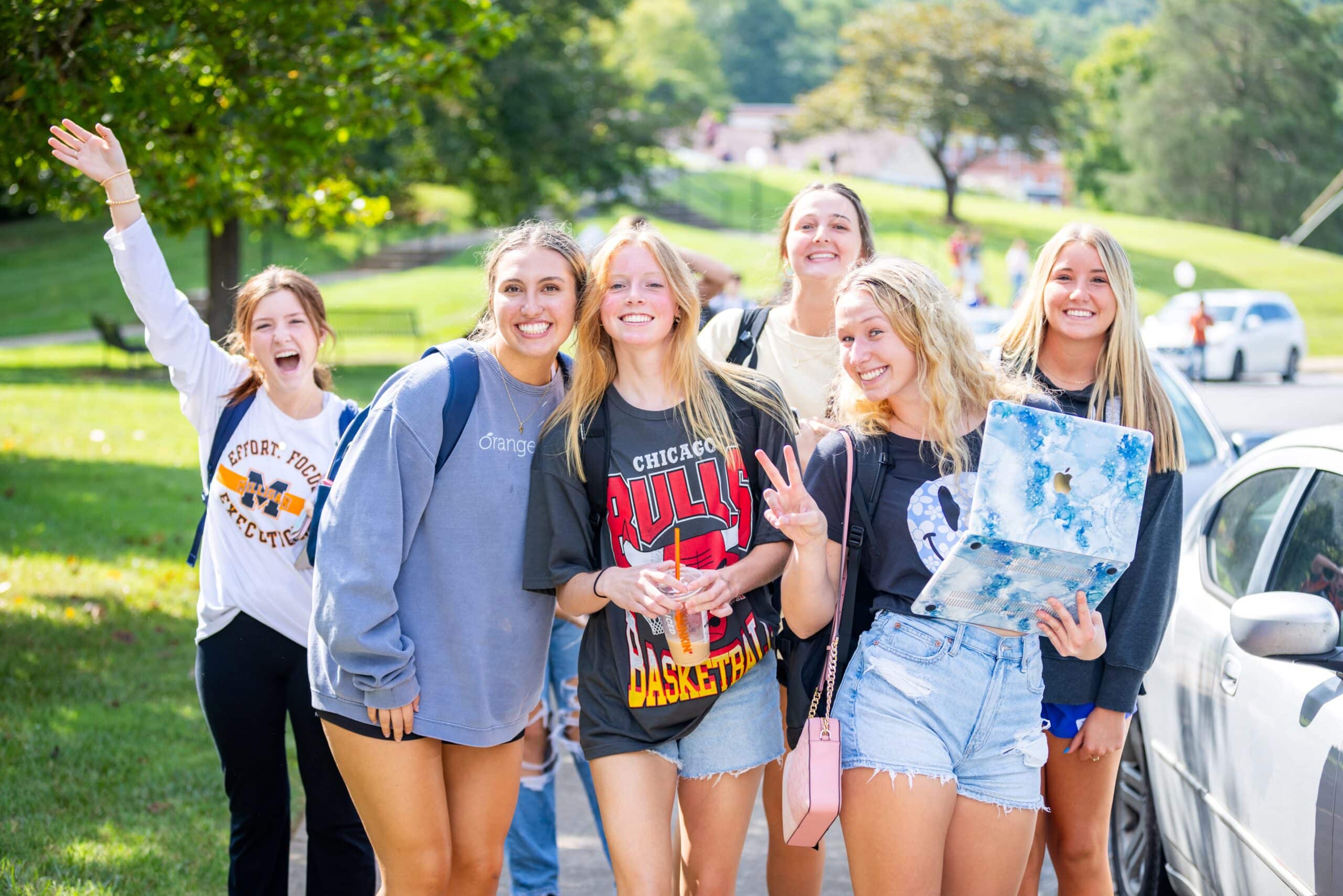 students gathered outside on a sunny day near a parked car